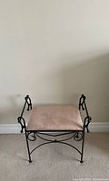 Small metal bench with beige upholstered seat cushion showing some staining. Iron frame with decorative scroll designs.