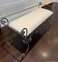 Angled view of upholstered metal bench showing scrollwork frame and fabric cushion