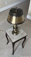 Full view of brass table lamp on top of the marble-top side table.