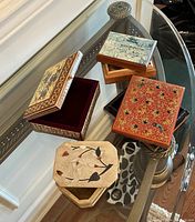 Photo showing a collection of decorative wooden boxes of various shapes and designs on a glass table
