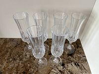 Six crystal champagne flutes standing on a granite countertop showing the cut and vertical etched designs