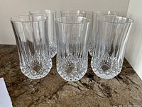 Set of 6 clear crystal highball glasses with diamond-cut and vertical ribbed designs shown grouped on counter.