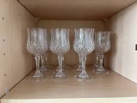 Set of 7 Crystal D’Arques Longchamp wine glasses displayed on wood shelf, showing diamond pattern and faceted stems.