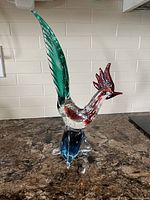 Front view of the Venetian glass rooster figurine showing red comb, clear body with bubbles, green tail, and blue base