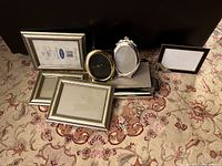 Photo showing 9 picture frames of various styles and sizes laid out on carpet.