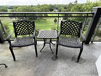 Two matching chairs flanking square lattice-pattern table on balcony