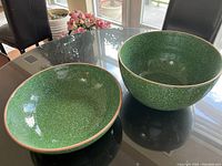Two green speckled ceramic bowls, one deep and one shallow, placed on a glass table for overall view.