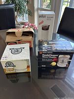 Four boxed small appliances grouped on a table including Braun Aromatic grinder, Black & Decker Handy Chopper, Mojave Kitchen Salt grinder, and another appliance in a brown box