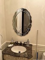 Full view of oblong Venetian mirror mounted above marble countertop sink, showing scalloped edges and clear floral etching on glass border.