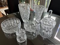 Overall view of seven assorted vintage pinwheel cut crystal pieces on a glass table.