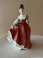 Front view of the Royal Doulton porcelain figurine showing the woman in a red dress with puffed sleeves, holding her gown.