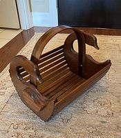 Wooden duck magazine rack showing carved duck head ends, slatted base, and curved handle on carpet