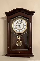 Front view of the wooden Bulova wall clock showing the clock face, pendulum, and the curved top wooden frame.