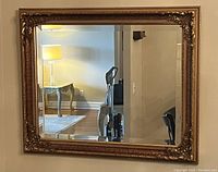 Full frontal view of the rectangular wall mirror hanging on the wall showing its reflective glass surface and ornate gold-toned frame with floral corners and bead detailing.