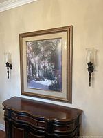Pair of decorative wall sconces mounted on a beige wall flanking a framed picture and placed above a wooden sideboard.