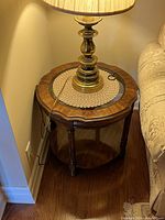 Side table with lamp showing the round wooden top with glass inset, crocheted doily, and a brass lamp base.