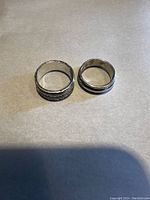 Two silver rotating rings placed side by side on a flat surface under natural light showing their rotating band design and condition.