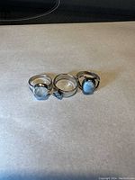 Three sterling silver rings displayed horizontally on a light background. The right ring features a blue larimar stone, the other two are silver design rings.