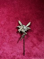 Photo of the front side of the 1960s brass fairy pin on a red velvet background showing detailed wings and seated fairy playing flute.