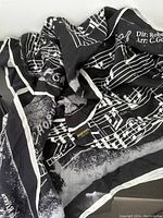 Black cotton scarf featuring white printed musical notes and arrangement text, shown crumpled to visualize fabric and pattern.