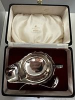 Sauce boat and ladle displayed in open fitted presentation case showing red velvet base and cream satin lid