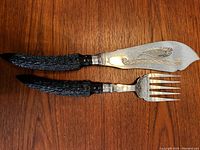 Fish serving set knife and fork with black textured handles, silver plate with fish engraving on knife blade.