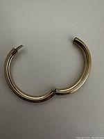 View of the open gold plated bangle, showing the hinged mechanism and curved tubular design.