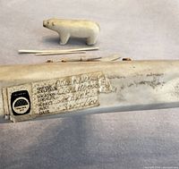 Polar bear figure and other bone carved items with handwritten label showing carver name, location (Coral Harbour), subject, and date (September 1980).