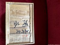 Wooden box with Japanese kanji writing on the lid, natural finish with some wood grain details visible.