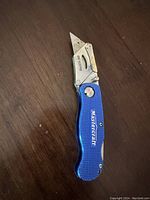 Photo of a Mastercraft utility knife with a blue aluminum handle, replaceable pointed blade partially extended, and a metal clip for pocket attachment.