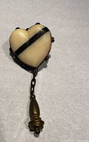 Front view of the heart-shaped carved mourning brooch with black diagonal stripe, encased in metal with black round decorative elements, attached to a chain and pendant drop.