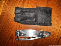 Closed multi-tool next to black fabric pouch on wooden surface.