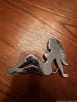 Front view of a metallic belt buckle featuring the silhouette of a reclining woman with long hair.