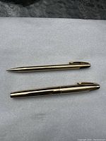 Gold tone Sheaffer 727 fountain pen and mechanical pencil, closed, showcasing exterior design and clips with white dot emblem.