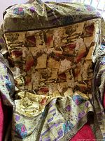 Photo of a multi-coloured silk scarf with an abstract, geometric pattern in shades of green, gold, purple, red, and brown. The scarf is draped over a chair to display its design and texture.