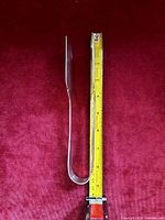 Side profile of the silver plate cake server placed on a red velvet surface with a tape measure next to it showing about 5 inches length.