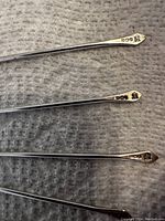 Close-up image showing the track of hallmarks on four sterling cocktail sticks, each with a small rooster design at the top, confirming authenticity and silver content.