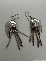 Front view of sterling silver kinetic dangle earrings with multiple cylindrical dangles attached to an irregular shaped metal base, showing hooks for ear attachment.