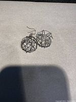 Photo showing two sterling silver wire earrings resembling tangled spherical cages, one missing a dangling component