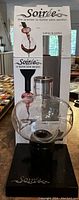 Front view of the Soirée wine aerator placed on its black stand, with original packaging behind it.