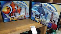 Photo showing both Air Swimmers Remote Control Kits boxes: Flying Clownfish and Flying Shark, displayed side by side on a wooden shelf.