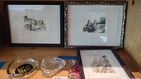Three framed black and white castle scene lithographs displayed against a wooden background. Two framed prints standing upright and one lying flat. Also visible are two glass ashtrays, noted not included in the sale.