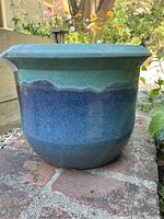 Front view of the blue-green glazed ceramic plant pot placed on a brick surface.