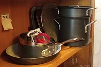 Photo showing one steamer pot, one Green Pan frying pan, one pot, cupcake pans, sifter, grater, and mini plastic juicer on a shelf.