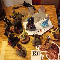 Photo showing the full set of approximately 12 Disney Infinity figurines on a wooden surface including a few on clear bases and one damaged with no head.