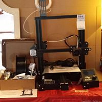 Ender-3 Pro 3D printer frame with power cable and guide book beneath, spool holder mounted on frame.