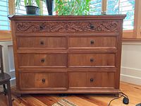 Front view of the dresser showing 8 drawers with one top carved drawer and glass top surface.