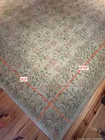 Photo showing corner of large rectangular rug with dimensions 12 feet by 17 feet marked, floral green and red swirl pattern on beige ground.