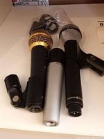 Three microphones laid on surface with one clip attached to mic and two clips in sealed bag