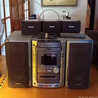 Front view of the Panasonic stereo system showing the central unit and two large speakers on either side with three smaller speakers behind.